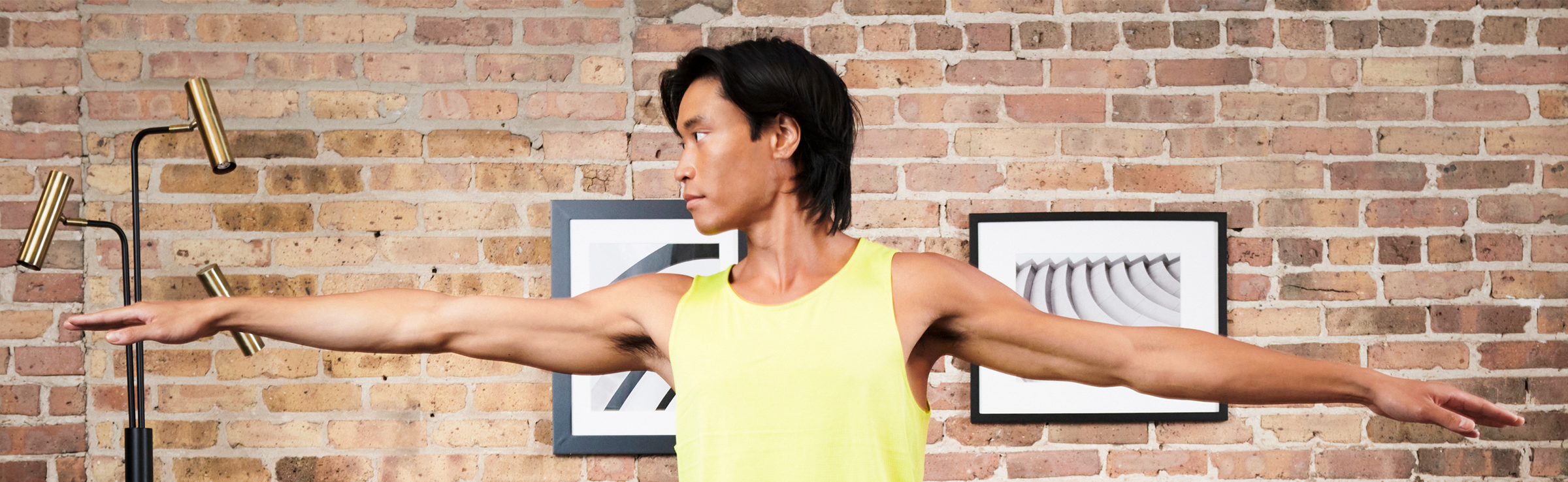 Male standing in yoga position Warrior 2 pose against brick wall residential interior background.